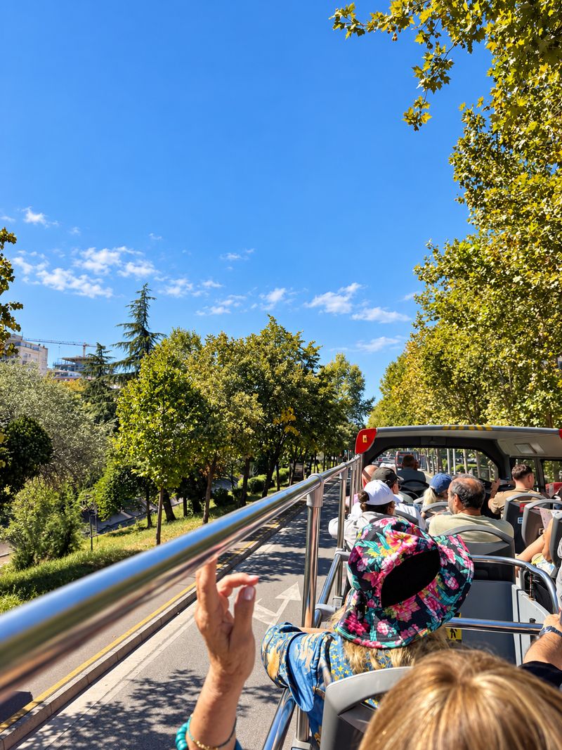 Open-top bus tour along a green boulevard in Tirana, Albania